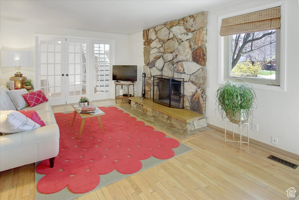 Living room with french doors, a stone fireplace, and light wood-type flooring