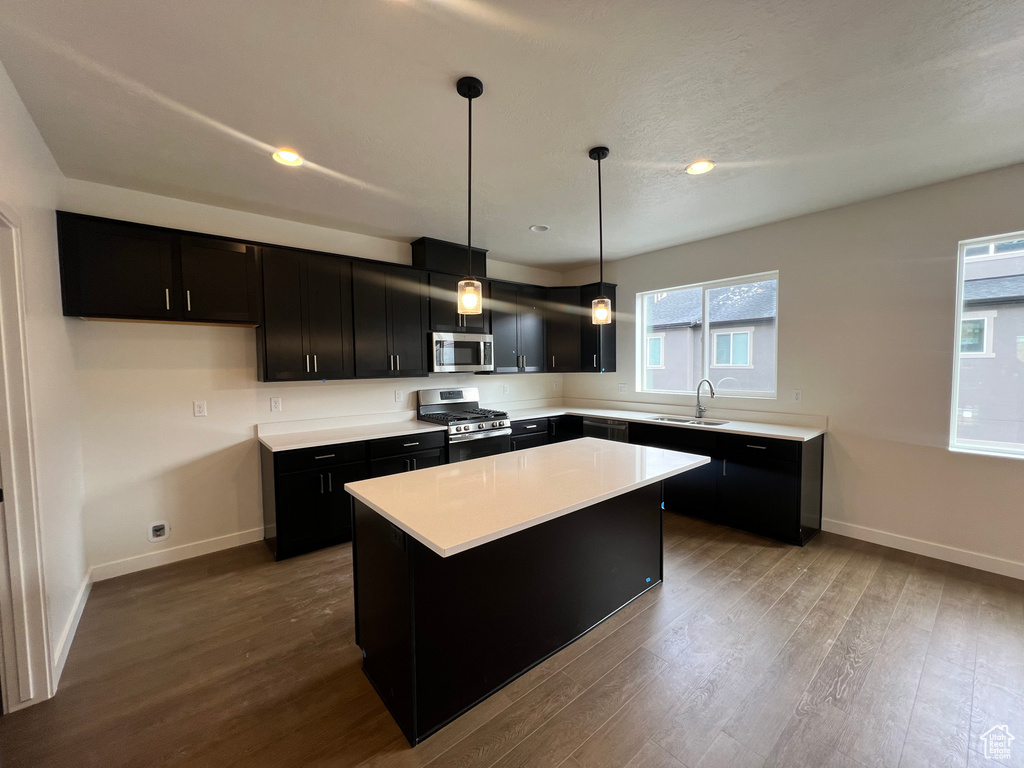 Kitchen featuring hardwood / wood-style flooring, decorative light fixtures, appliances with stainless steel finishes, and a center island