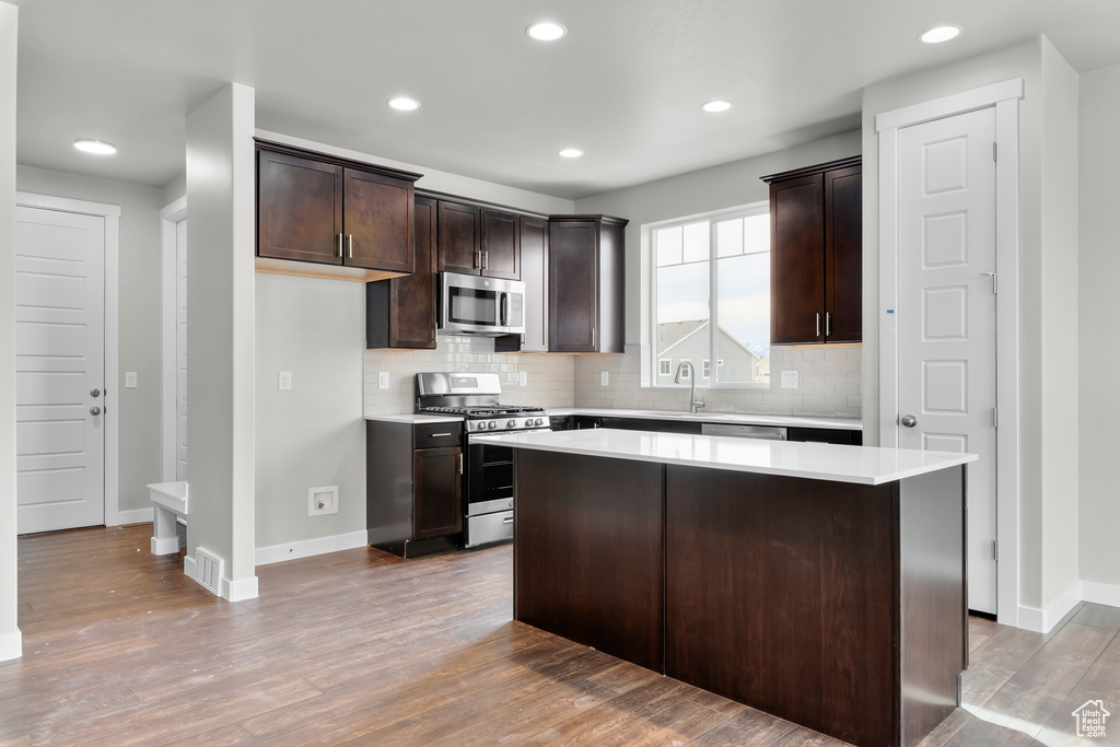 Kitchen with appliances with stainless steel finishes, dark brown cabinetry, a center island, tasteful backsplash, and wood-type flooring