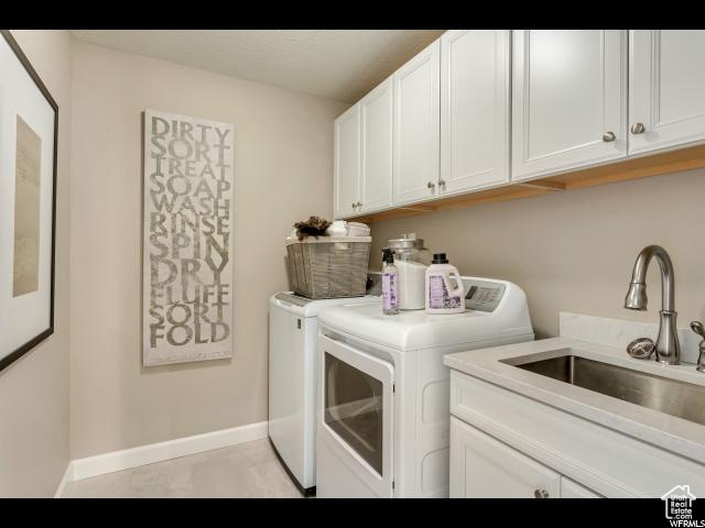 Laundry room with cabinets, light tile flooring, sink, and washer and clothes dryer