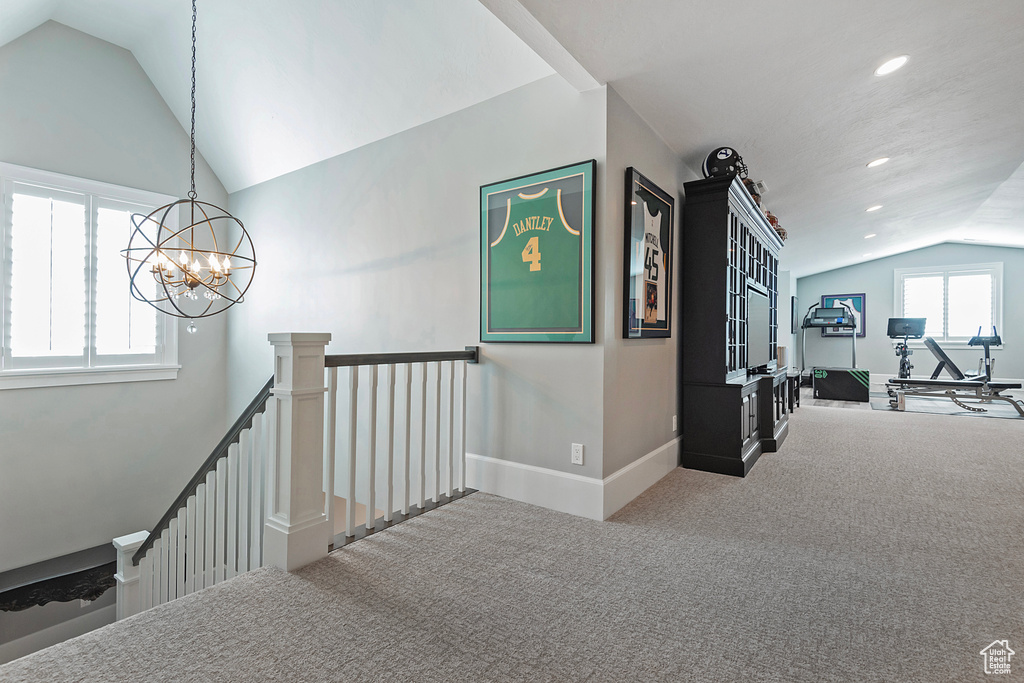 Hallway with vaulted ceiling, light carpet, and a notable chandelier