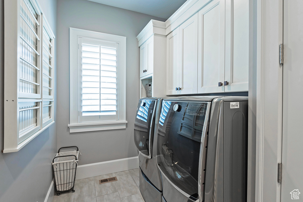 Washroom with washer and dryer, plenty of natural light, light tile floors, and cabinets