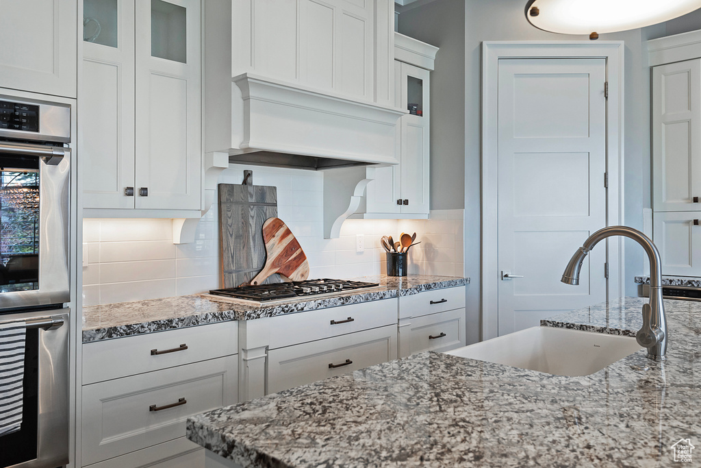 Kitchen featuring premium range hood, white cabinets, tasteful backsplash, and stainless steel appliances