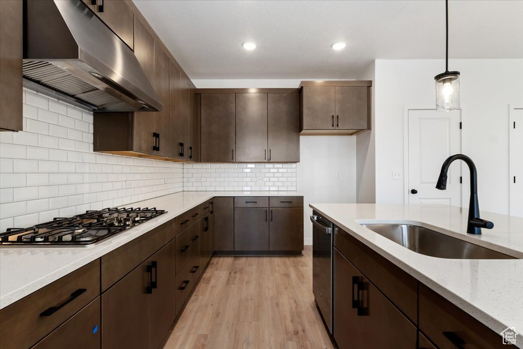 Kitchen with wall chimney range hood, light stone counters, pendant lighting, tasteful backsplash, and light hardwood / wood-style flooring