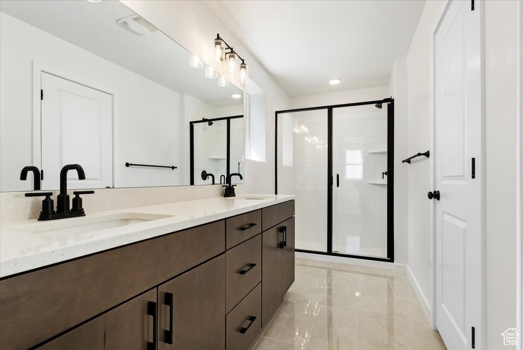 Bathroom featuring large vanity, a shower with door, double sink, and tile floors