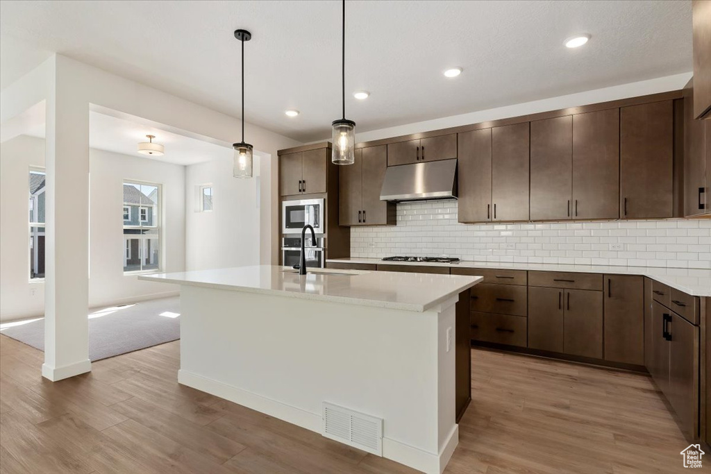 Kitchen featuring light hardwood / wood-style floors, a center island with sink, tasteful backsplash, and stainless steel microwave