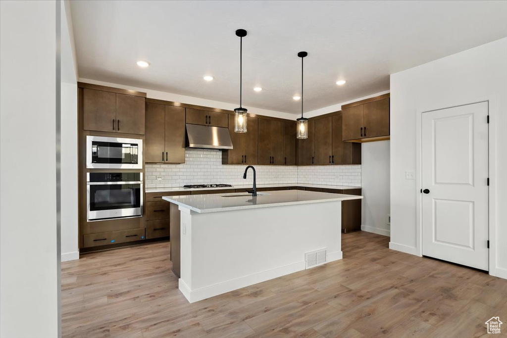 Kitchen featuring a kitchen island with sink, light wood-type flooring, stainless steel appliances, and pendant lighting