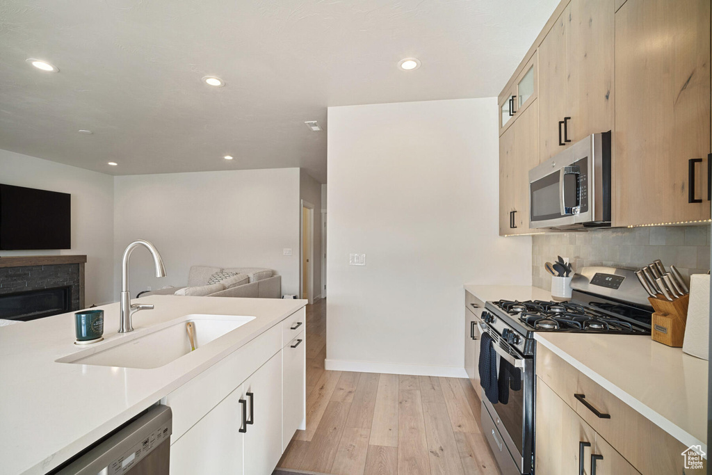 Kitchen featuring sink, light wood-type flooring, stainless steel appliances, tasteful backsplash, and light brown cabinets