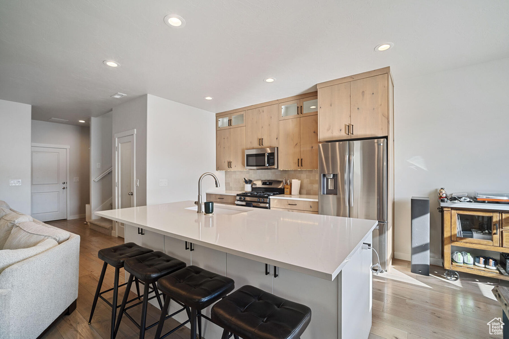 Kitchen with backsplash, light hardwood / wood-style floors, stainless steel appliances, a breakfast bar area, and sink