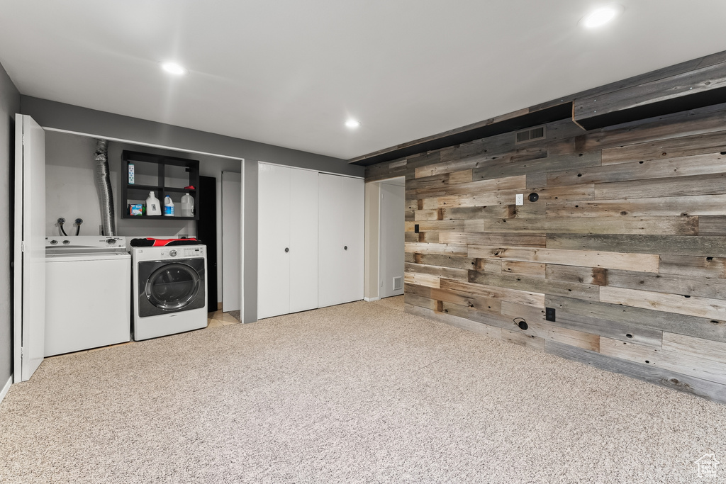 Basement featuring washing machine and clothes dryer, light carpet, and wooden walls