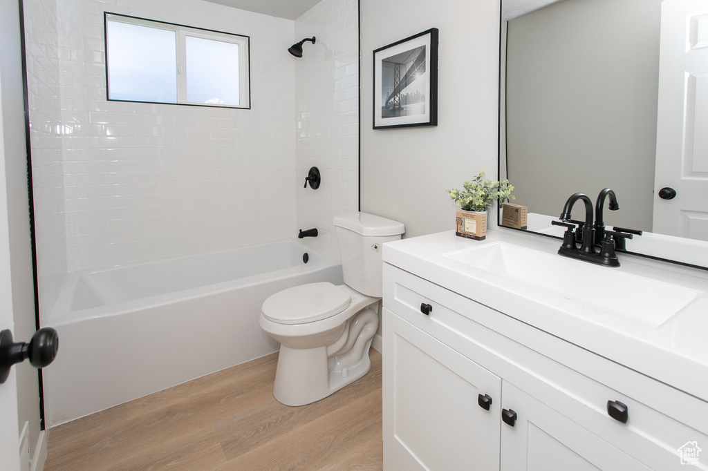 Full bathroom with tiled shower / bath combo, vanity, toilet, and hardwood / wood-style flooring