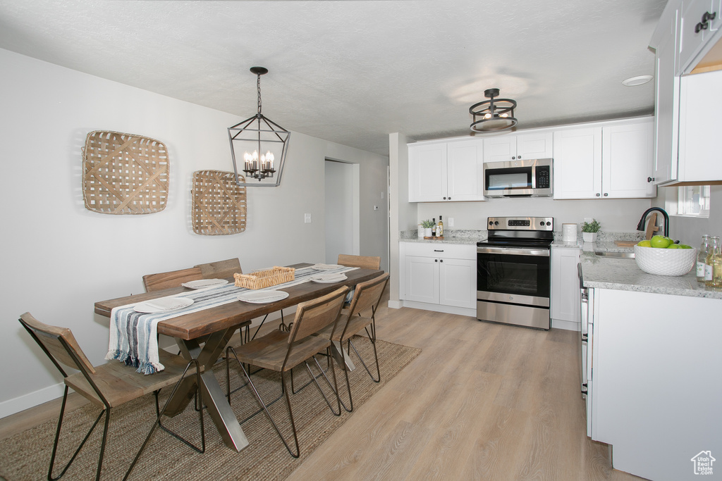 Kitchen with a notable chandelier, white cabinetry, appliances with stainless steel finishes, and light hardwood / wood-style flooring