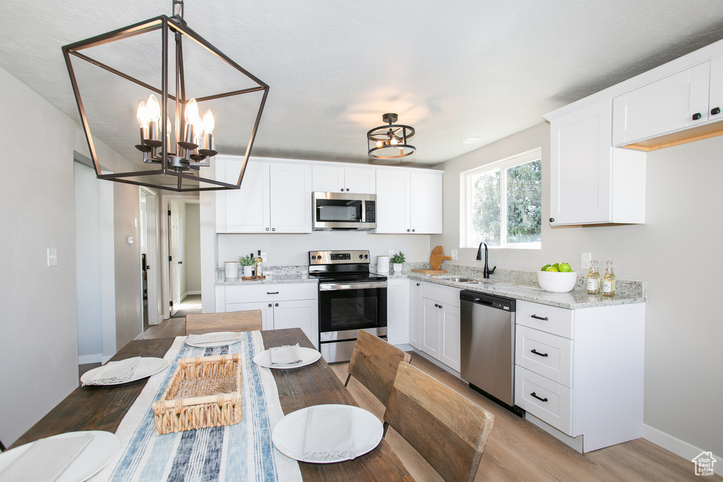 Kitchen with white cabinets, appliances with stainless steel finishes, sink, and a notable chandelier