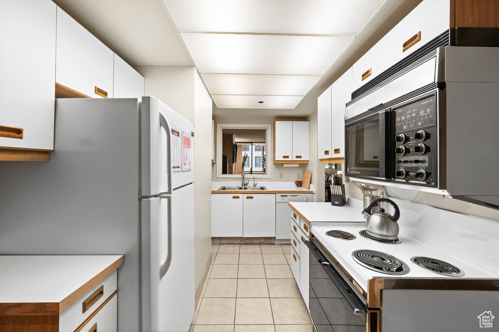 Kitchen featuring white cabinets, white appliances, light tile floors, and sink