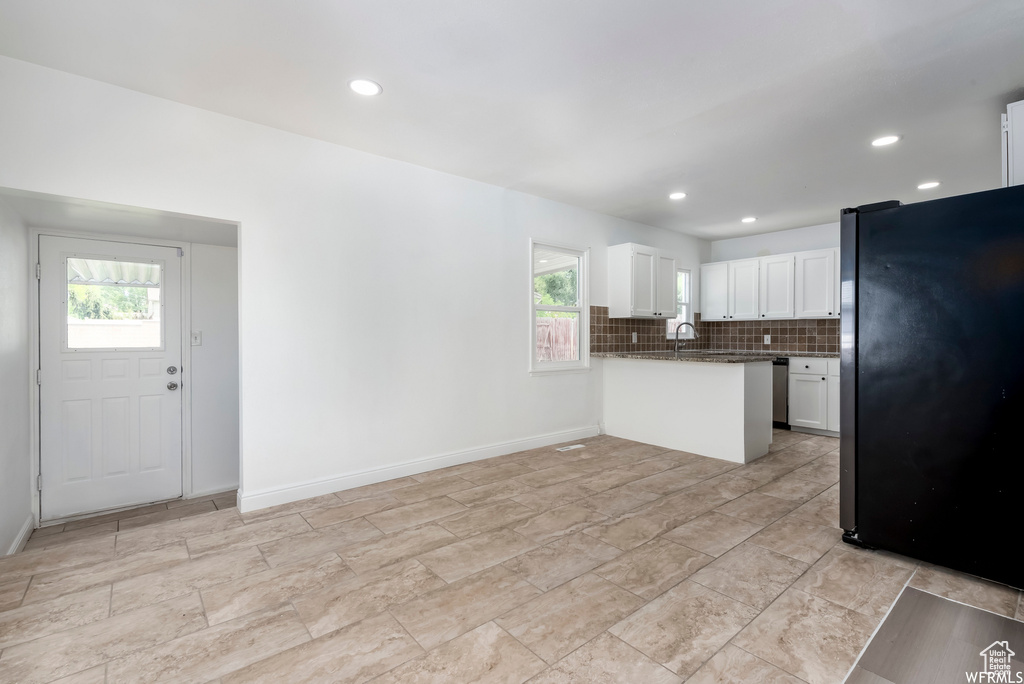 Kitchen with black fridge, light tile flooring, backsplash, and white cabinetry