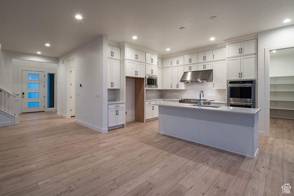 Kitchen featuring appliances with stainless steel finishes, light hardwood / wood-style flooring, a center island with sink, and white cabinetry