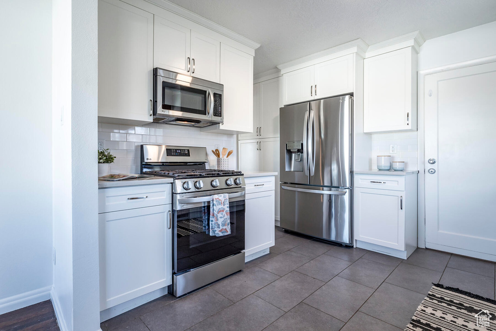 Kitchen with dark tile floors, white cabinetry, appliances with stainless steel finishes, and tasteful backsplash