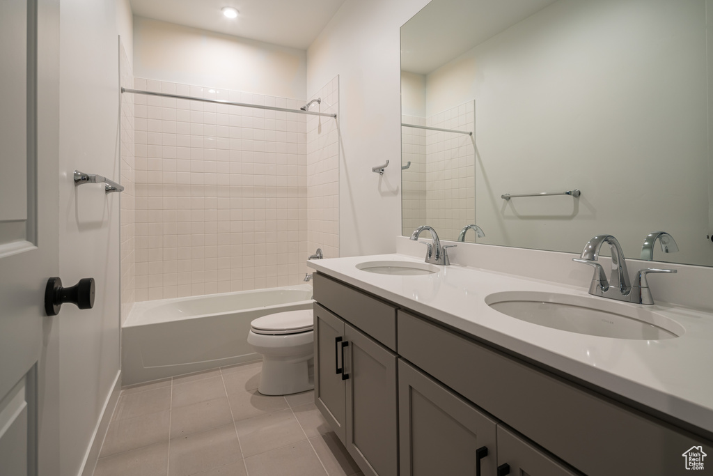 Full bathroom featuring dual bowl vanity, tiled shower / bath combo, tile flooring, and toilet