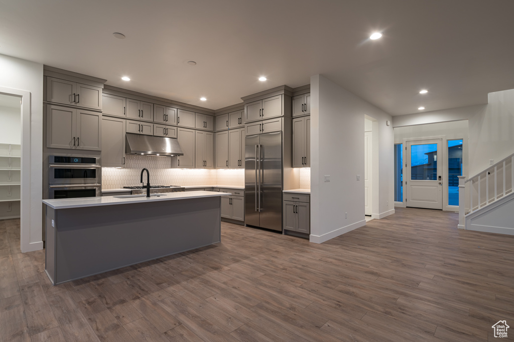 Kitchen featuring stainless steel appliances, an island with sink, and dark hardwood / wood-style flooring