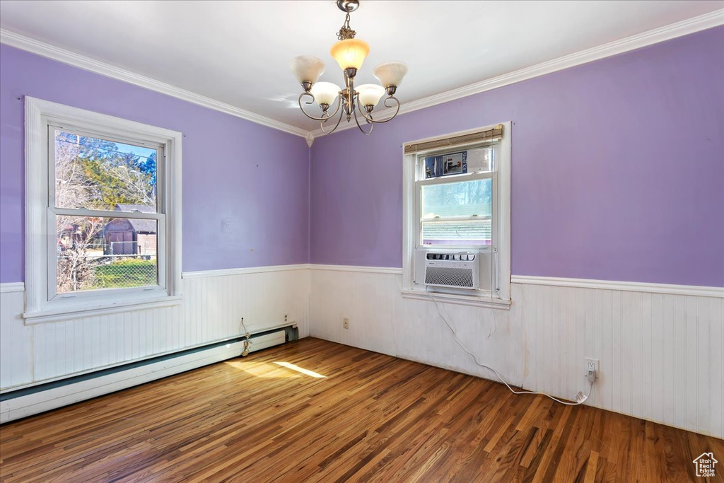 Empty room with a baseboard radiator, ornamental molding, dark wood-type flooring, and a chandelier