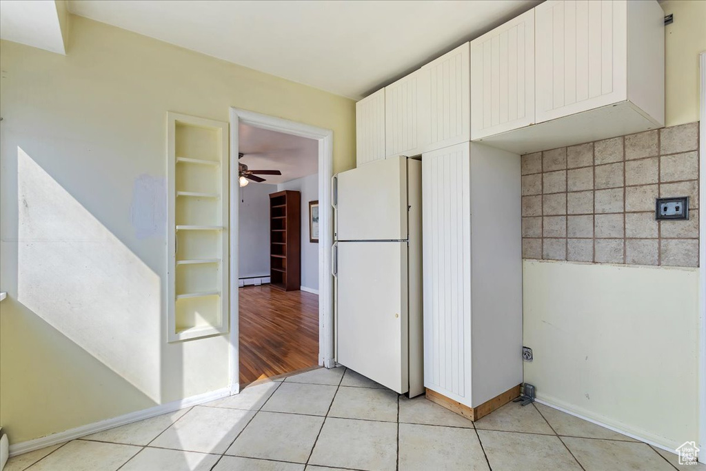 Kitchen with a baseboard heating unit, backsplash, white fridge, light tile floors, and ceiling fan
