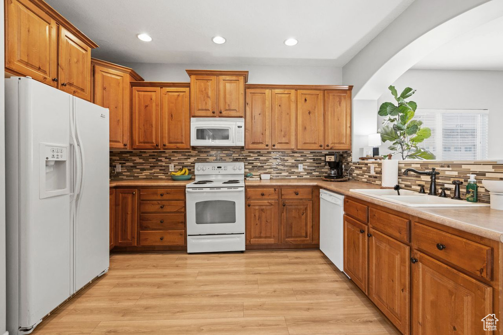 Kitchen with tasteful backsplash, white appliances, and light wood-type flooring
