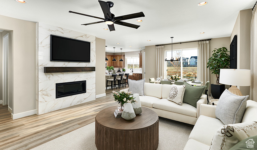 Living room featuring ceiling fan with notable chandelier, a premium fireplace, and light wood-type flooring