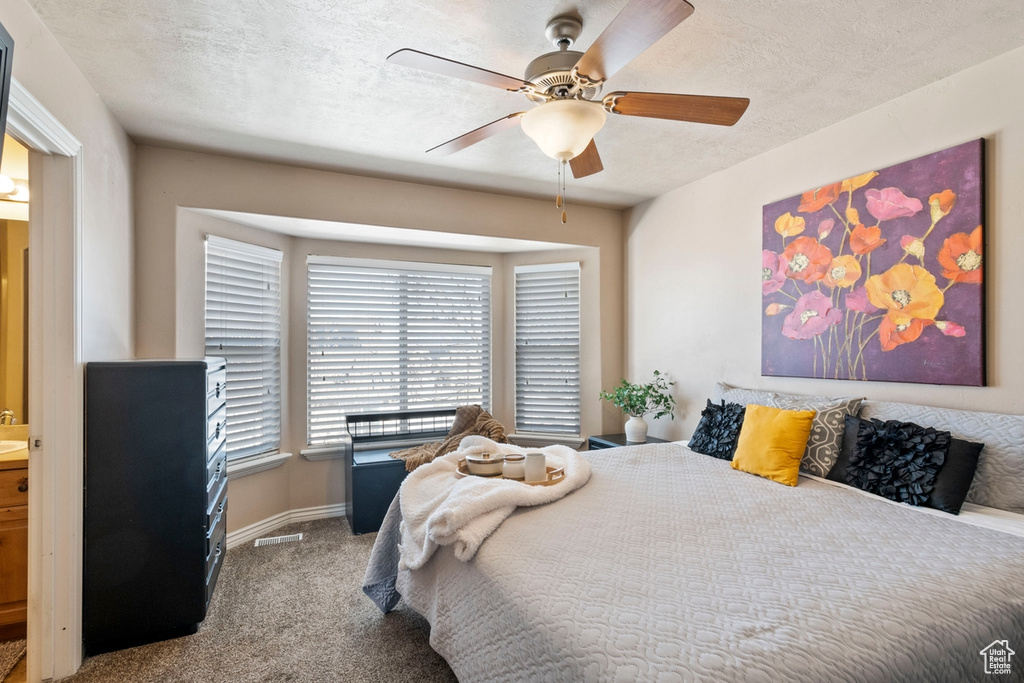 Bedroom featuring a textured ceiling, ensuite bath, light carpet, and ceiling fan