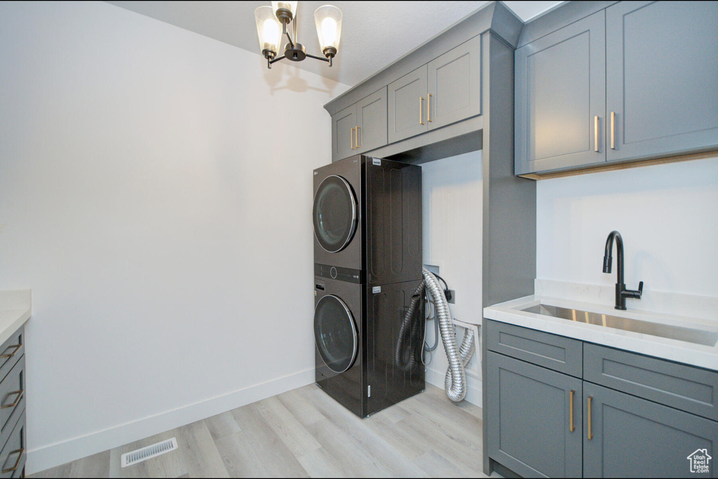 Washroom featuring stacked washer and dryer, an inviting chandelier, sink, light hardwood / wood-style flooring, and cabinets