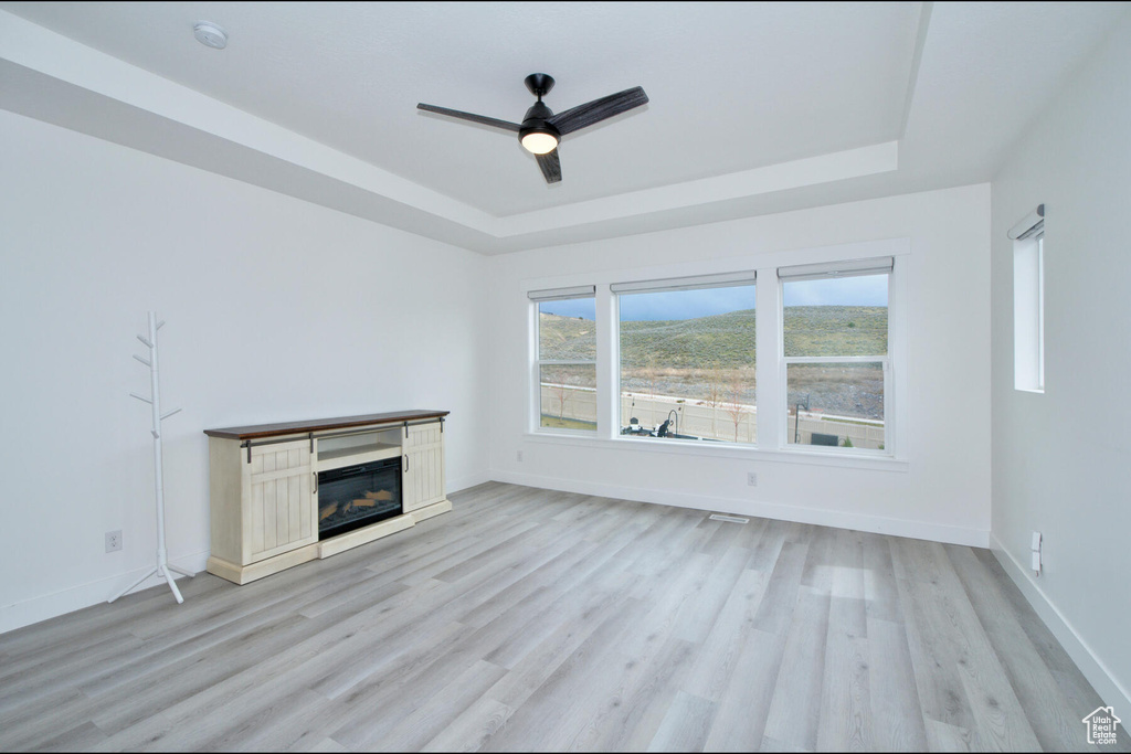 Unfurnished living room with a tray ceiling, ceiling fan, and light hardwood / wood-style flooring