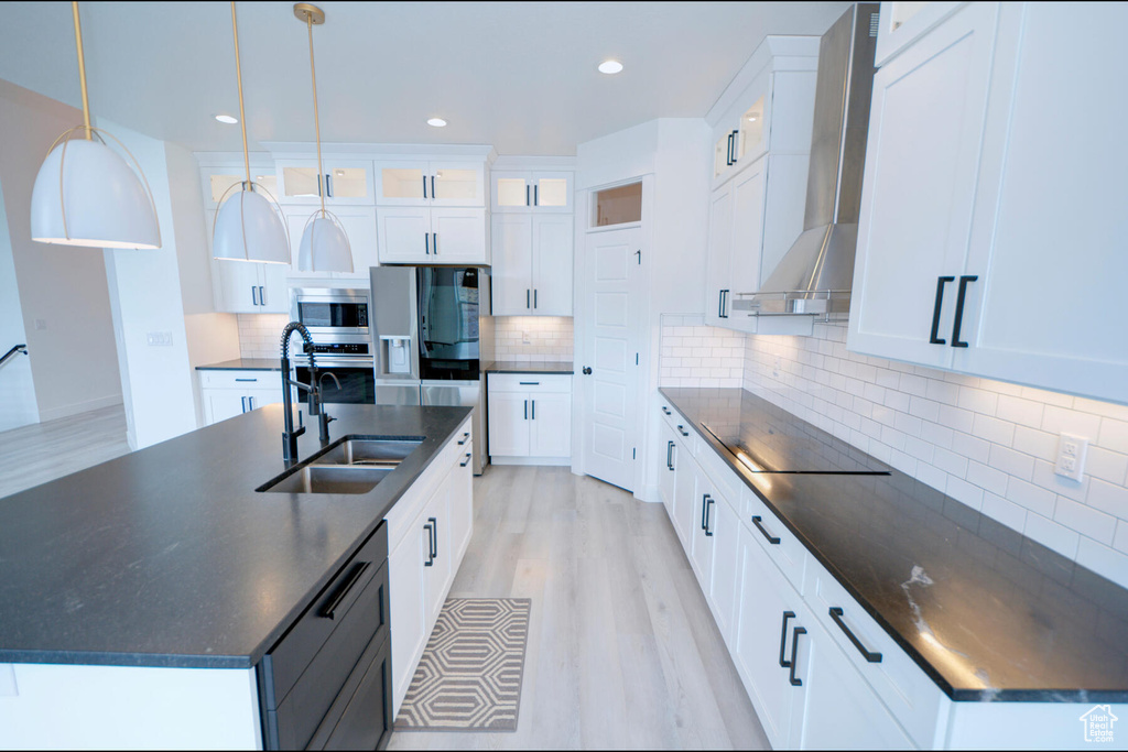 Kitchen featuring backsplash, light wood-type flooring, wall chimney exhaust hood, and sink