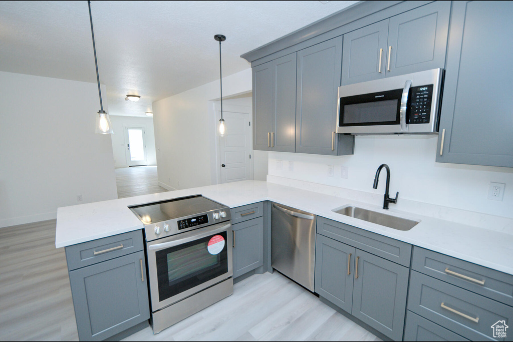 Kitchen featuring appliances with stainless steel finishes, hanging light fixtures, light hardwood / wood-style flooring, and sink