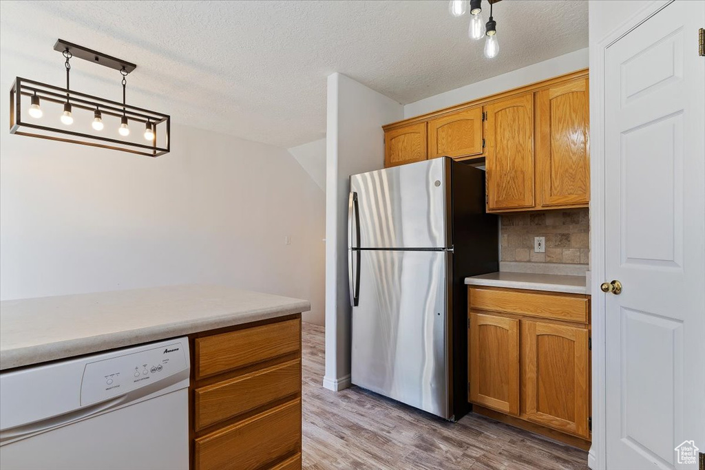 Kitchen featuring light wood-type flooring, rail lighting, stainless steel fridge, tasteful backsplash, and white dishwasher