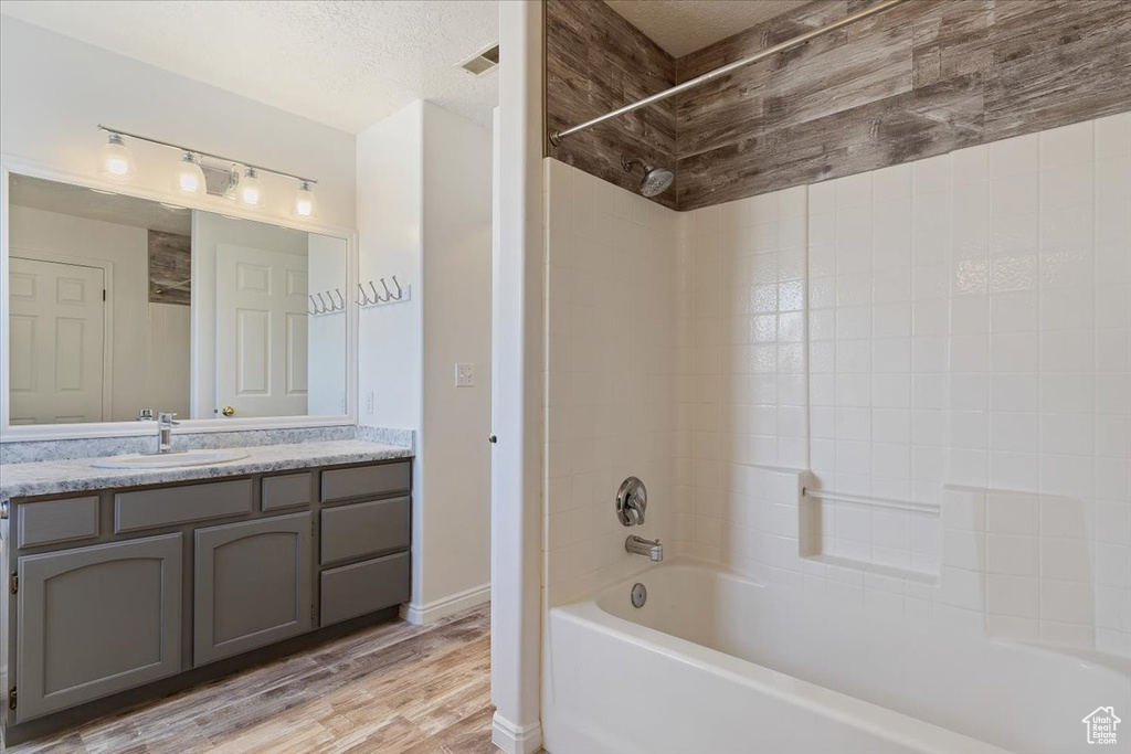 Bathroom featuring a textured ceiling, vanity, washtub / shower combination, and hardwood / wood-style flooring