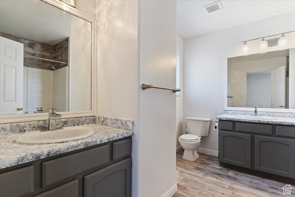 Bathroom with a textured ceiling, hardwood / wood-style floors, large vanity, and toilet