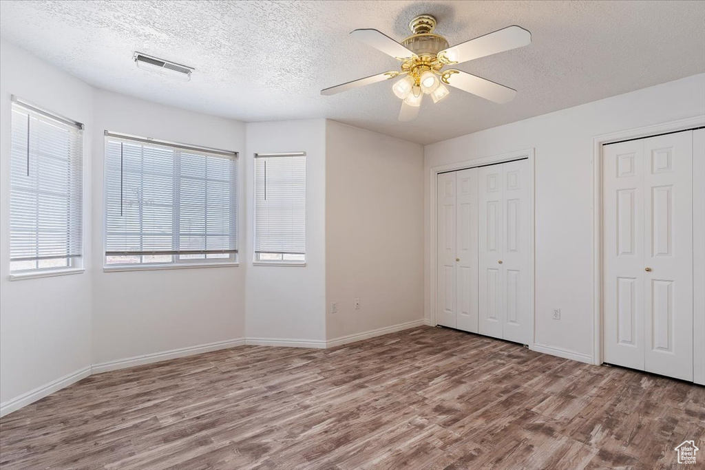 Unfurnished bedroom with multiple closets, dark wood-type flooring, and ceiling fan