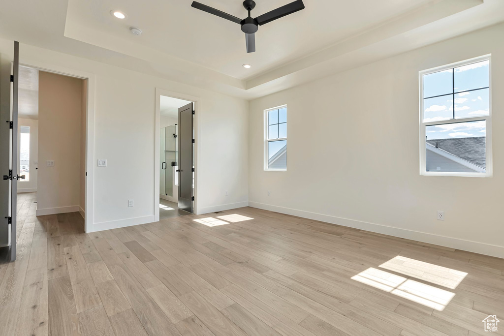 Unfurnished bedroom featuring ceiling fan, a tray ceiling, and light hardwood / wood-style floors