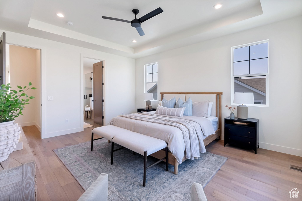 Bedroom with light hardwood / wood-style flooring, connected bathroom, and a raised ceiling