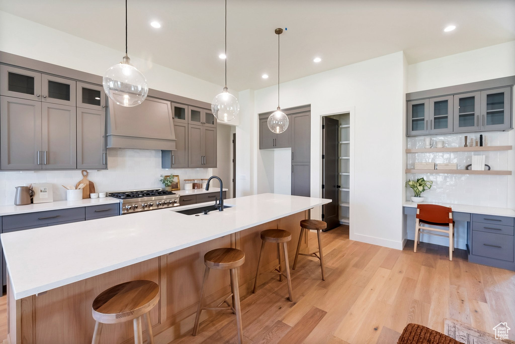 Kitchen featuring premium range hood, an island with sink, sink, stove, and light hardwood / wood-style flooring