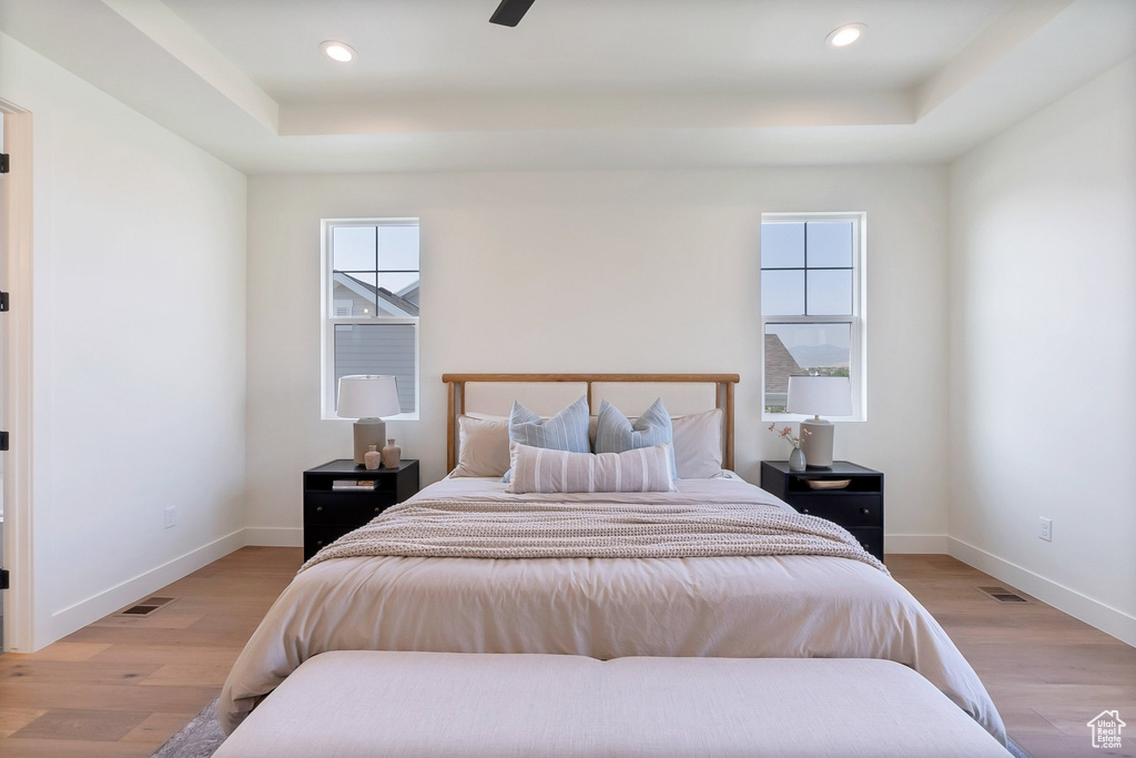 Bedroom with light hardwood / wood-style floors, ceiling fan, and a raised ceiling