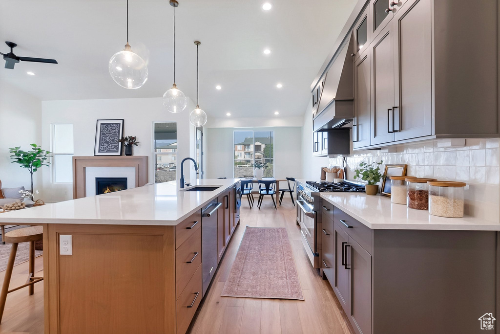 Kitchen with light hardwood / wood-style flooring, double oven range, backsplash, ceiling fan, and a spacious island