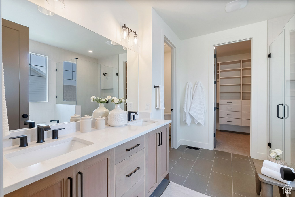 Bathroom featuring double vanity, tile patterned flooring, and a shower with door