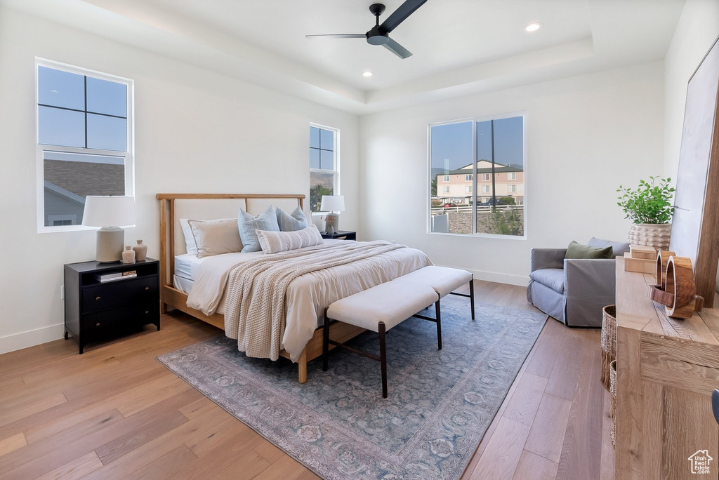 Bedroom featuring ceiling fan, multiple windows, light wood-type flooring, and a tray ceiling