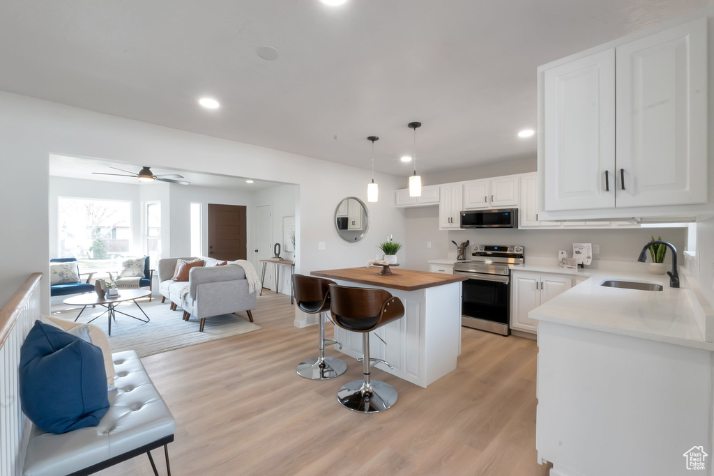 Kitchen featuring electric range, white cabinets, light hardwood / wood-style flooring, sink, and decorative light fixtures