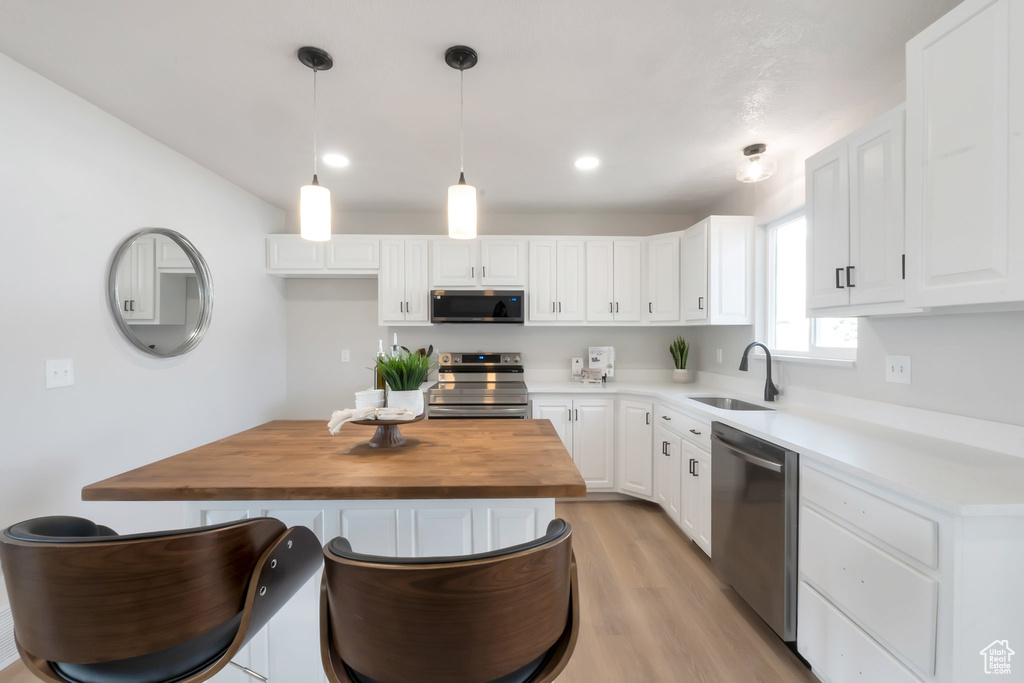 Kitchen featuring white cabinets, sink, decorative light fixtures, appliances with stainless steel finishes, and a center island