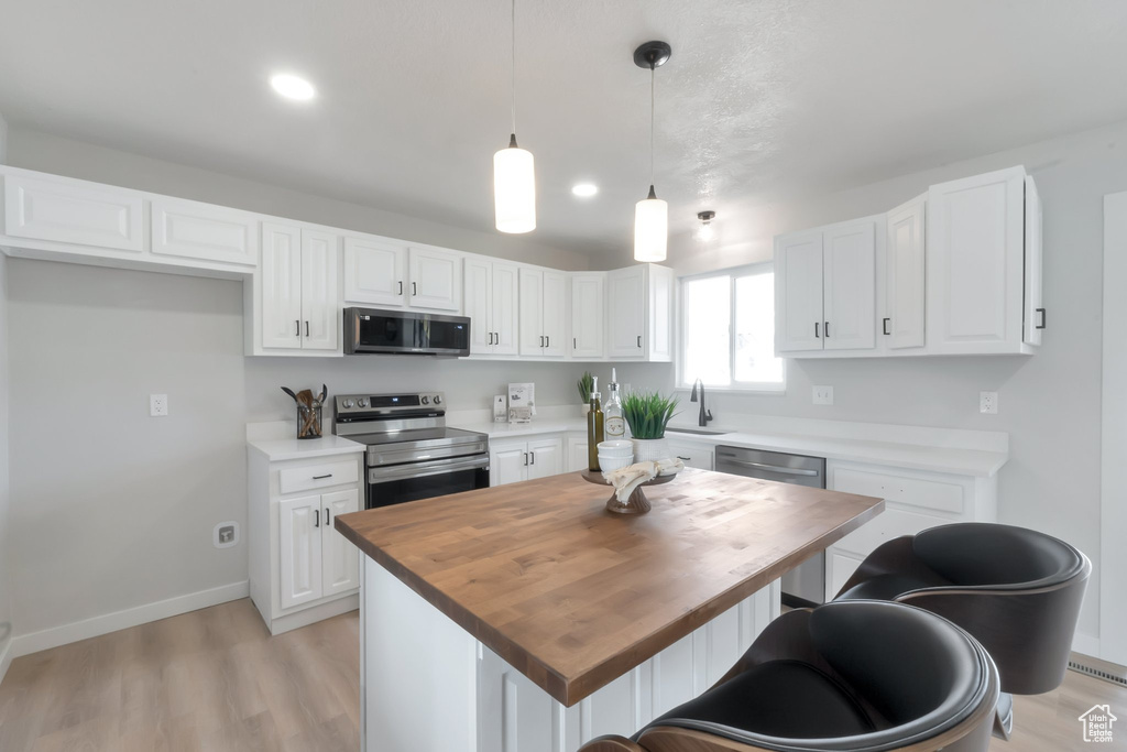 Kitchen featuring pendant lighting, light hardwood / wood-style flooring, appliances with stainless steel finishes, a center island, and white cabinetry