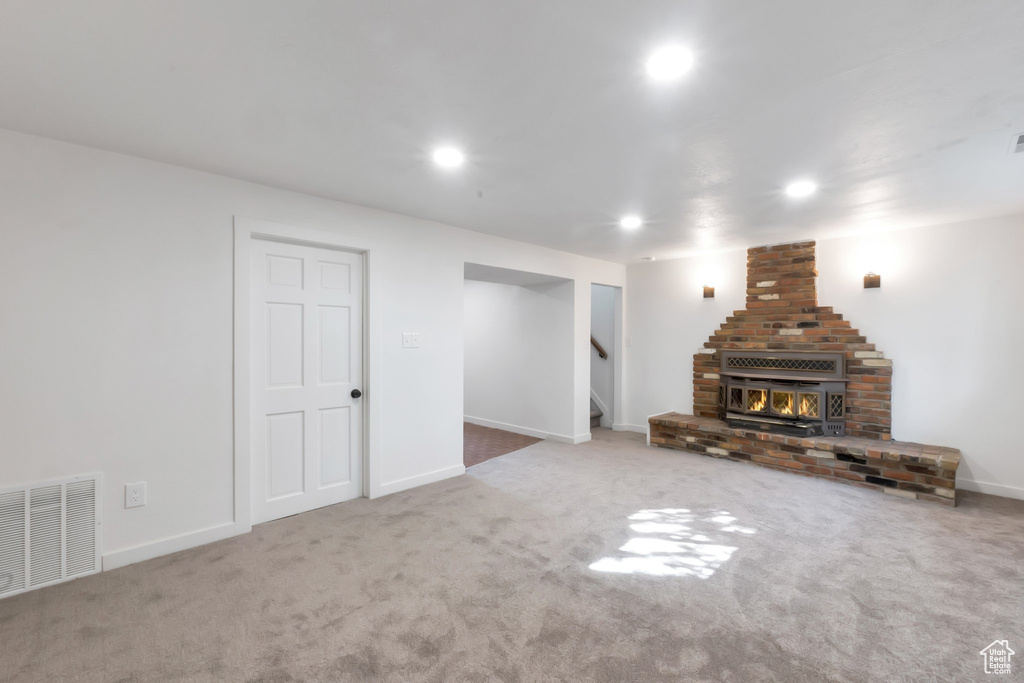 Unfurnished living room featuring light colored carpet, brick wall, and a fireplace