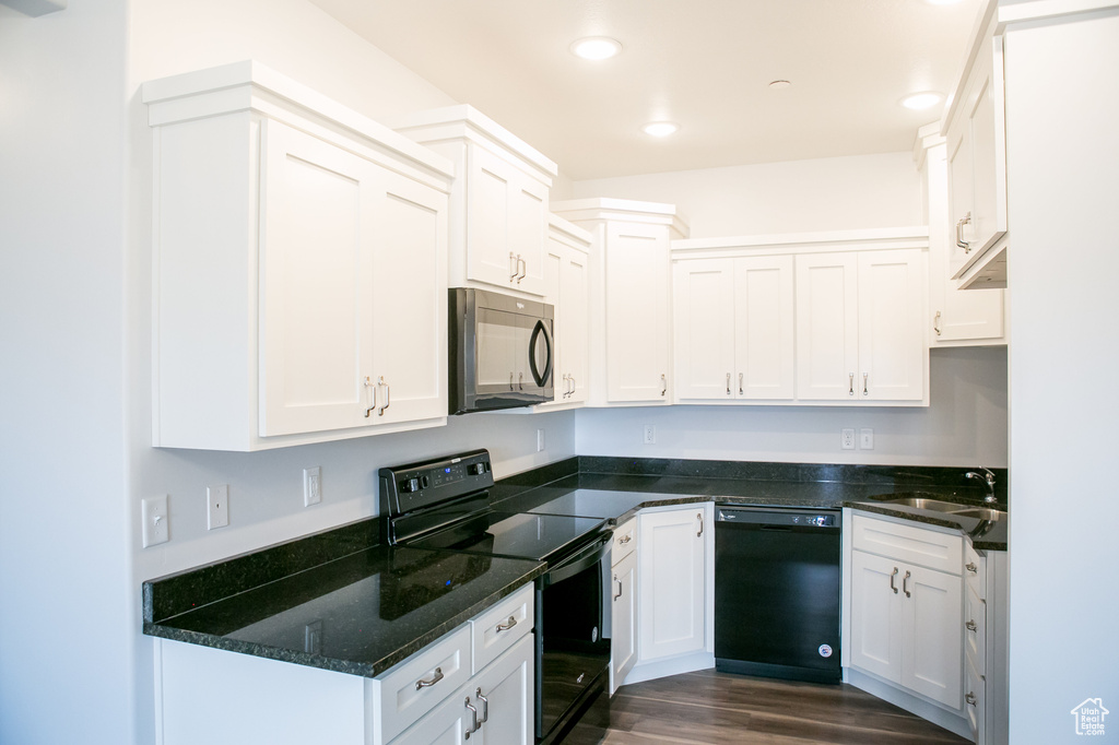 Kitchen featuring dark hardwood / wood-style floors, sink, black appliances, white cabinetry, and dark stone counters
