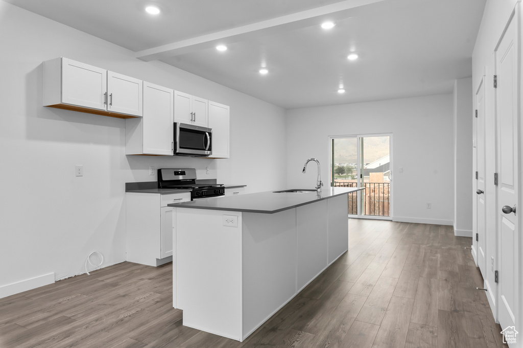 Kitchen featuring appliances with stainless steel finishes, white cabinets, sink, light wood-type flooring, and a center island with sink