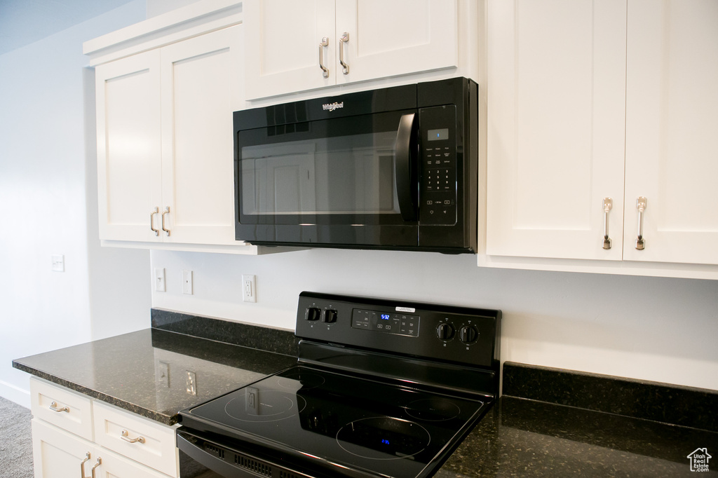 Kitchen with dark stone counters, white cabinetry, and black appliances